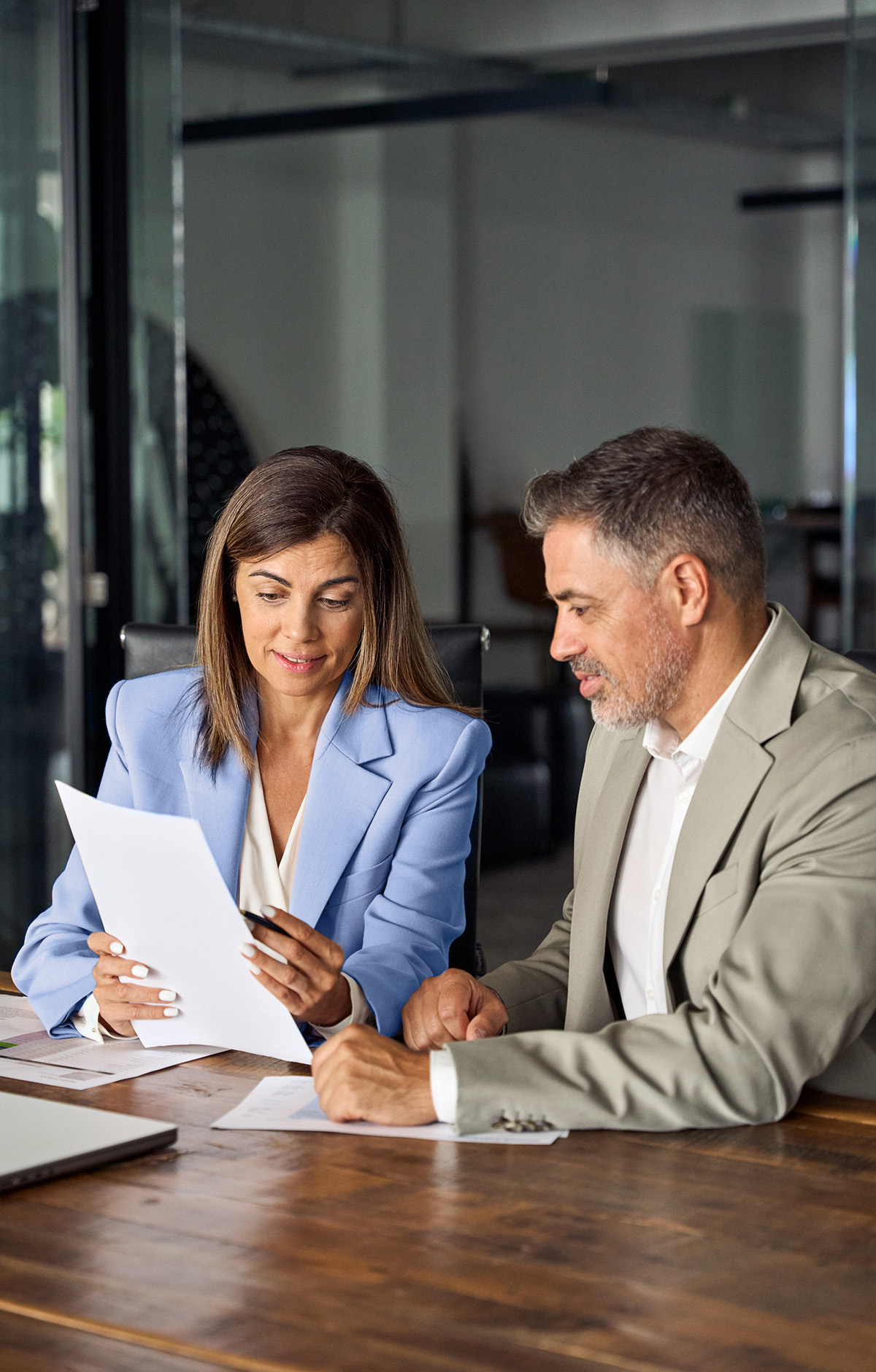 Two legal professionals, one male, one female, discussing a document at a boardroom table